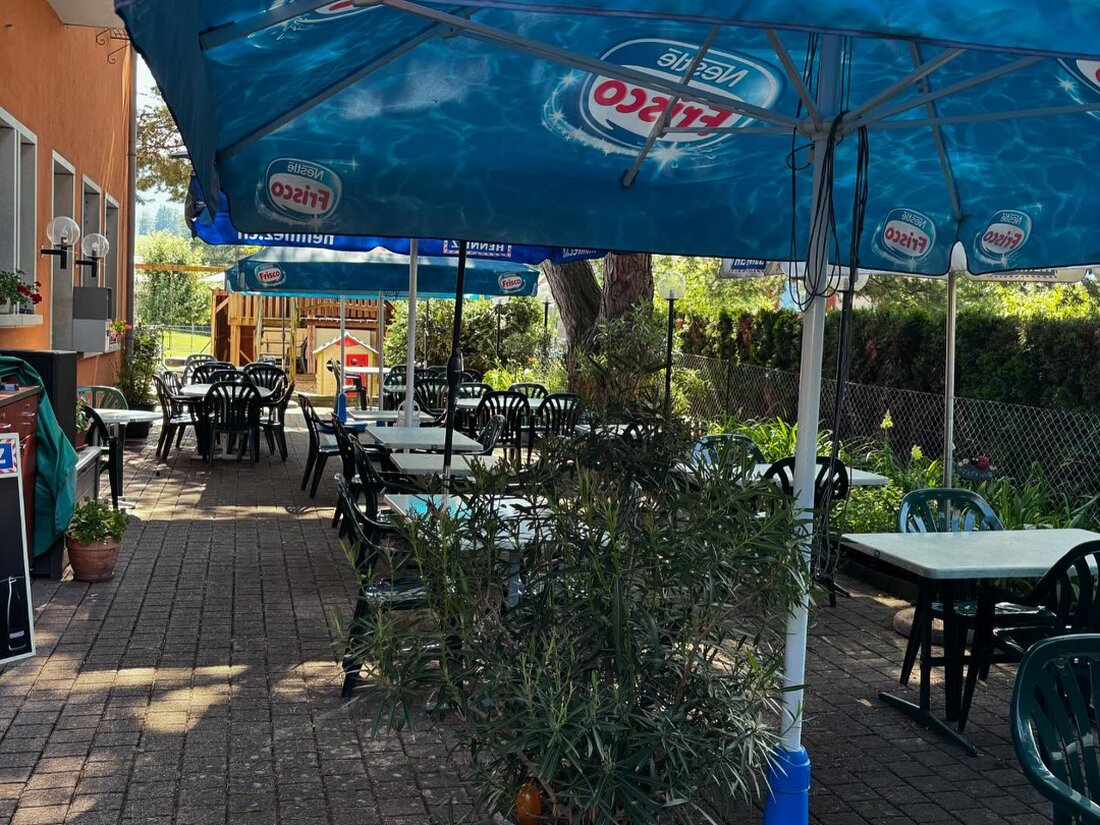 Terrasse du restaurant avec tables dressées à l’ombre des parasols avec détsailplace de jeux pour enfants